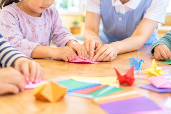 折り紙を一緒に折る子どもと職員の手元